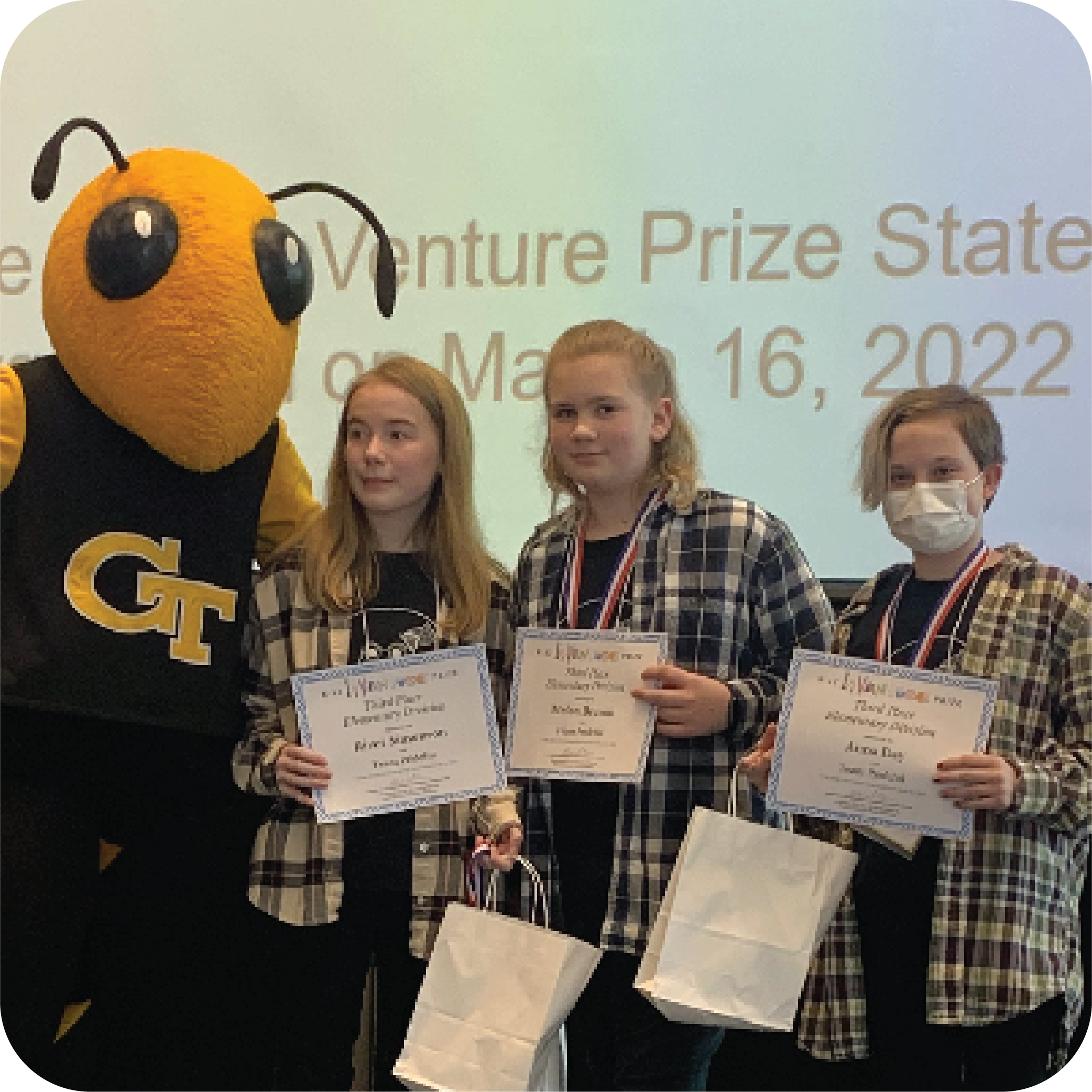 Three smiling students holding certificates and standing next to Buzz (Georgia Tech's yellowjacket mascot).